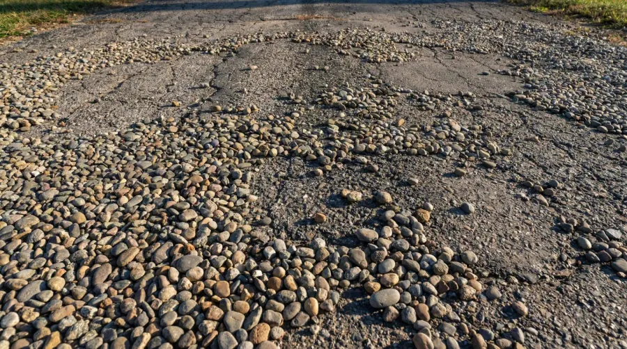 Scattered pebbles on asphalt driveway creating uneven surface