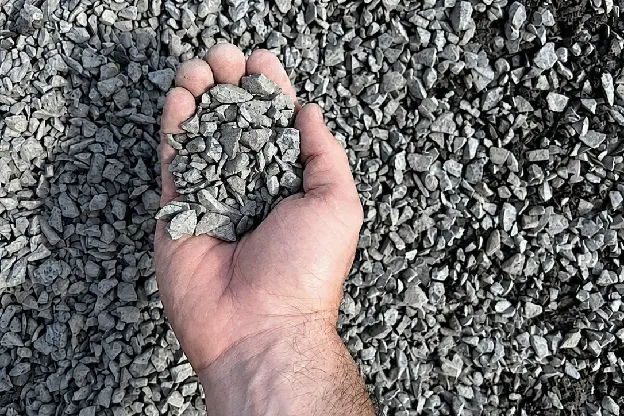 Handful of angular 3/8 inch crushed stone held above a pile of crushed stone