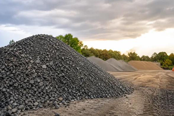 Stockpile of dark grey crushed road base at a materials yard at dusk