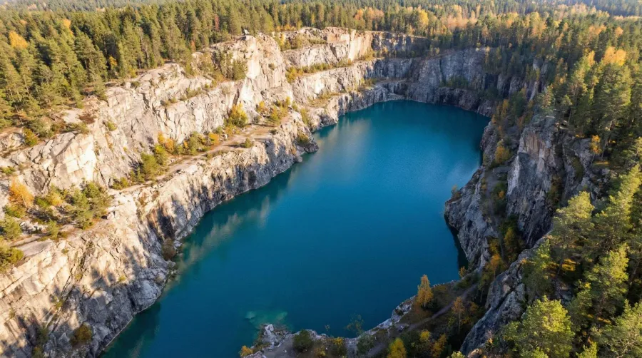 Aerial View Of Water Filled Quarry With Blue Water Surrounded By Rocky Walls