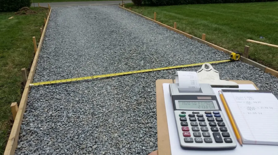 crushed stone driveway with measuring tape and calculator showing calculation process