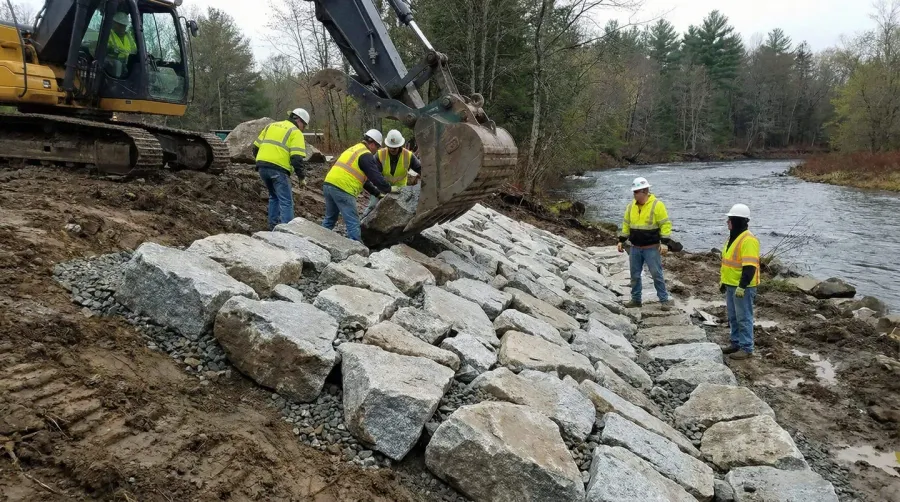 Construction crew placing Class II rip rap stones along a streambank with proper spacing and interlocking arrangement