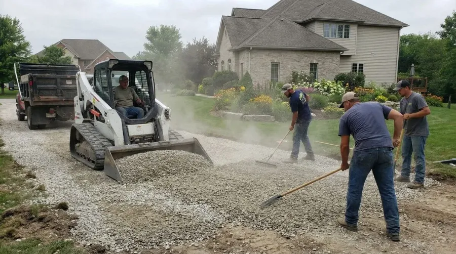 Workers spreading limestone gravel on a driveway during installation