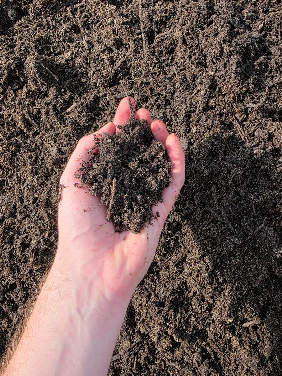Mound of dark garden soil beside a planted raised bed and a wheelbarrow