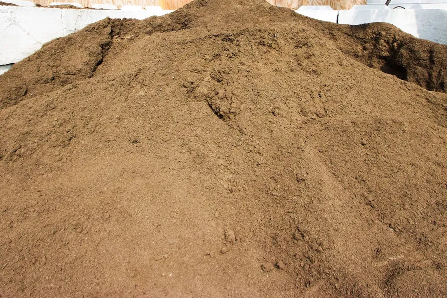 Handful of dark, crumbly topsoil held above a bed of screened soil