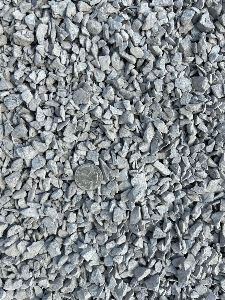 Handful of angular 3/8 inch crushed stone held above a pile of crushed stone